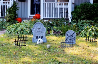 Front yard of private house decorated by fake skull, bones hands, tombstones and grates, pumpkins on the porch for a old american trick-or-treat Hallo