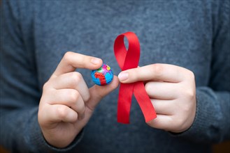 World day of fight against AIDS. The symbols are a red ribbon and an imitation of a globe in the hands of a person. This day is intended for all
