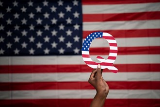 Hands holding Q alphabet with US flag as background with copy space - Concept QAnon or Q Anon deep state conspiracy theory
