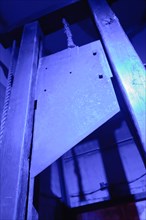 Blade of a guillotine lit with blue light