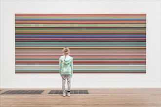 A girl stands in front of a large Bridget Riley painting in the Tate Modern Art Gallery.