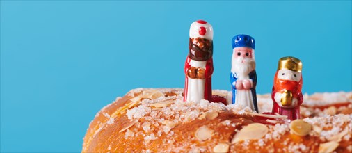 the three wise men, melchior, caspar and balthazar, on top of a roscon de reyes, the spanish king cake, on a blue background in a panoramic format to