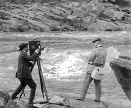 Archival Photo: A man with a film camera filming Senator Miles Poindexter fishing ca. 1918-1920