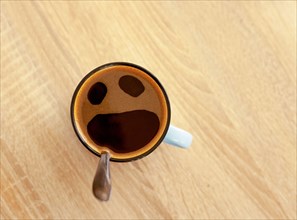 Coffee cup with funny screaming in fear face, top view. Open crying mouth in mug on table background. Shocked, stressed, angry, scared and furious foa