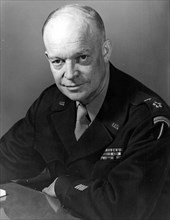 Half-length portrait of Dwight Eisenhower, seated with arms leaning on a table, with a serious facial expression, wearing black military shirt, 1945.