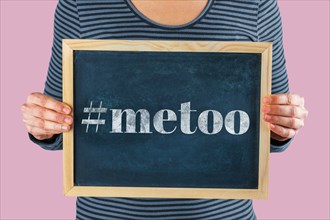Female hands holding small black chalkboard in front of the body with written words saying #metoo