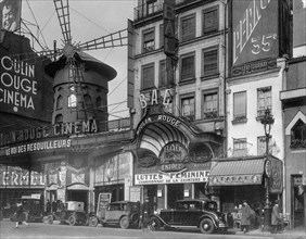 An early twentieth century black and white photograph showing the Moulin Rouge in Paris, France. Also shows the Moulin Rouge Cinema and cars of the era.