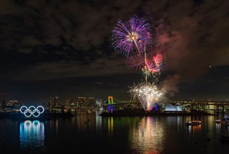 A picture of the fireworks commemorating the opening of the Olympic Rings in the Tokyo Bay, featuring the Rainbow Bridge, at night (Tokyo).