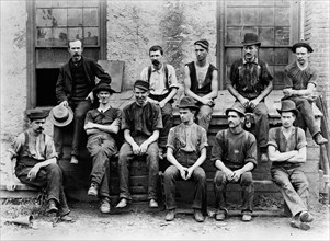 1890s 1900s GROUP OF 11 FACTORY WORKERS SEATED OUTSIDE OF BUILDING