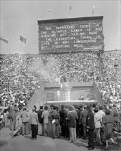 Olympic Games. London. 1948. The Olympic Flame being lit by the final torch bearer John Mark. A quote from Baron de Coubertin on the giant scoreboard behind.