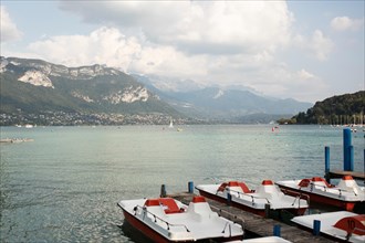 Paddle boats for rent line Lake Annecy looking toward the Alps in Annecy, France.