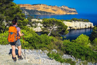Sporty hiker woman with backpack enjoying the view with blue water bay from the hiking trail in Calanques National Park, Cassis, Provence, France, Eur