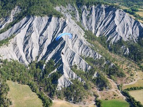 AIR-TO-AIR VIEW. Paraglider soaring above a landscape of eroded ravines. Barcelonnette, Alpes-de-Haute-Provence, France.