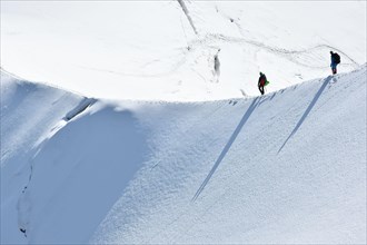 Trekkers hiking up a snowy ridge on White Valley, Mont Blanc massif from Aiguille du Midi 3842m, Chamonix, France