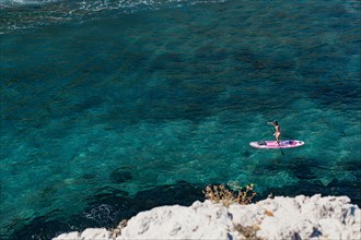 A woman is enjoying a session on a stand up paddle SUP on crystal clear waters in the South of France in Summer