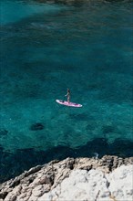 A woman is enjoying a session on a stand up paddle SUP on crystal clear waters in the South of France in Summer