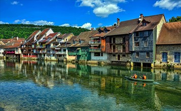 Canoe navigation along the Loue river which is overlooked by the characteristic houses. Town of Ornans in the Doubs department, Burgundy-Franche-Comte