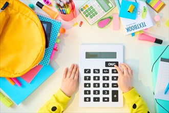 Back to school. Upper view of modern child with workbooks, stationary, textbook, calculator and backpack at white table at home.