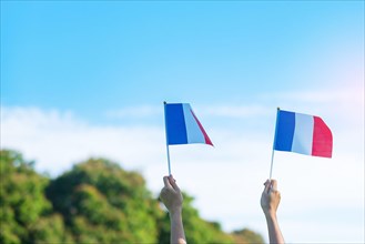 hand holding France flag on blue sky background. holiday of French National Day, Bastille Day and happy celebration concepts