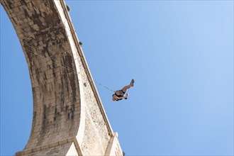 Low angle view of a person swinging after bungee jumping from a historic stone bridge. Adventure sports concept. Space for text