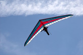 Hang gliding pilot flying blue red and white hang glider against sky in mountains of French Alps Haute Savoie France