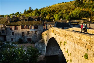 Walker in evening sunlight crossing the bridge at le Pont de Montvert on the Robert Louis Stevenson Trail Lozère, France