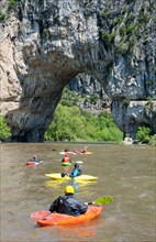People canoeing on the Ardeche river in the canyon Gorges d'Ardèche near a natural rock bridge near Vallon-Pont-d'Arc, France