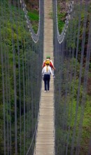 two hikers walking a suspension bridge, France, Mercantour National Park, Lantosque