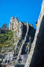 Rock climber in yellow climbing in canyon with castle beyond