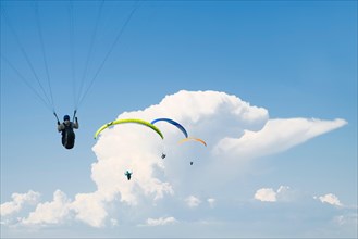 Four paragliders in a  row in front of cumulus clouds and a blue sky at Lake Annecy,France