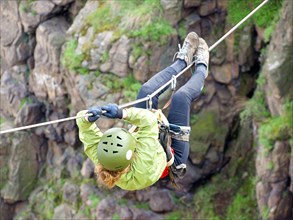 A female climber crosses a gorge along a tyrolean traverse