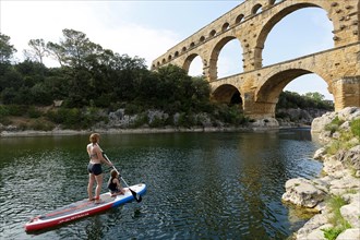 Mother and son stand up paddling (SUP) on the Gardon river and Pont du Gard, Provence, France.