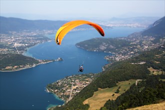 A tandem pilot and his passenger flying in front of Col de la Forclaz takeoff with lake Annecy in the background