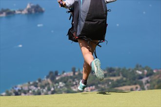 A female paragliding pilot taking off at Col de la Forclaz, near Annecy, France, with Lake Annecy in the background.