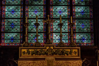 Alter candles in brass candler holders with a  stunning blue and green stained glass window behind in Notre Dame Cathedral ,Paris