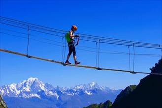 woman crossing a simple suspension bridge, Via Ferrata of La Plagne, Mont Blanc in background, France, Savoie, Tarentaise