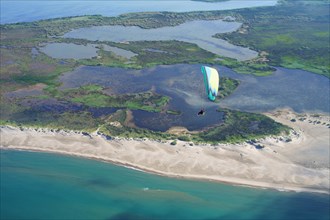 AERIAL VIEW. Paramotorist flying above a landscape of marshlands alongside the seacoast. Camargue marshes of the Rhone Delta, Arles, Provence, France.