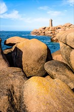 The Ploumanac'h lighthouse, named Mean Ruz, on the Pink Granite Coast in Perros-Guirec, northern Brittany, with large granite rocks in the foreground.