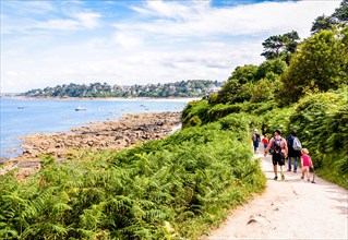 A family with children is walking towards Perros-Guirec on the "sentier des douaniers", the GR34 coastal path along the Pink Granite Coast in Brittany