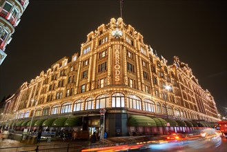 Exterior view of Harrods Department Store in London at night during Winter period. Night traffic street scenery in a typical rainy day.