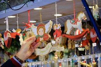 Man's hand grabbing cute christmas ornament with "Joyeux Noel" hanging on display from a stall, amongst other ornaments at the Strasbourg Christmas Ma