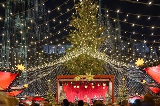 Night view of Weihnachtsmarkt, Christmas Market, with decorated illuminate stalls surround big Christmas tree at plaza in front of Cologne Cathedral.