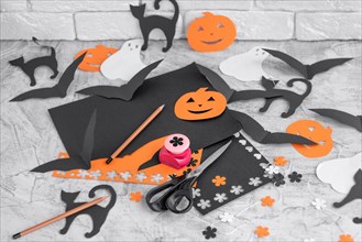 Decoration for the holidays, cutting from colored paper on a white concrete table. Preparation for Halloween. Orange and black colored paper, scissors, pencils, figured hole punch. Toned. Soft focus.