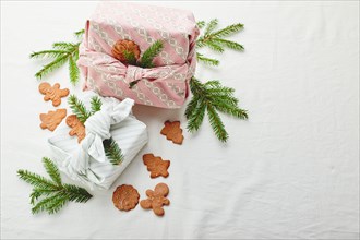 Christmas eco-friendly gift wrap in traditional japanese furoshiki style decorated with fir twigs and gingerbread cookies on fabric background, eco-fr