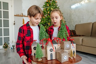 Children opening Christmas handmade advent calendar in a house shape to countdown the days until Christmas in the room.