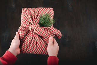 Children's hands holding gift wrapping in natural fabric in the style of Furoshiki. Sustainable gifts. Zero waste. Xmas eco holiday. High quality phot