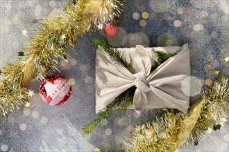 Furoshiki style gift for Christmas or New Year on a gray background with bokeh. Flat lay with balls and tinsel.