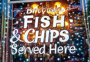 Fish and chips sign warm welcoming with frosty snow effect in winter, sign on traditional London pub window with welcoming warm festive twinkling lights at night Traditional British food in winter ser...