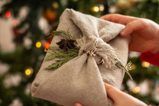 Christmas sustainable gifts .Children's hands hold eco-friendly gift wrapping in the traditional Japanese furoshiki style on the background of a Chris