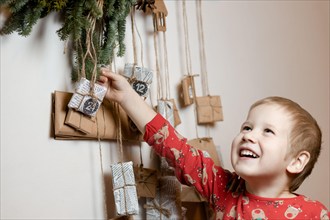 Smiling little boy taking gift from Advent calendar at home. Christmas tradition